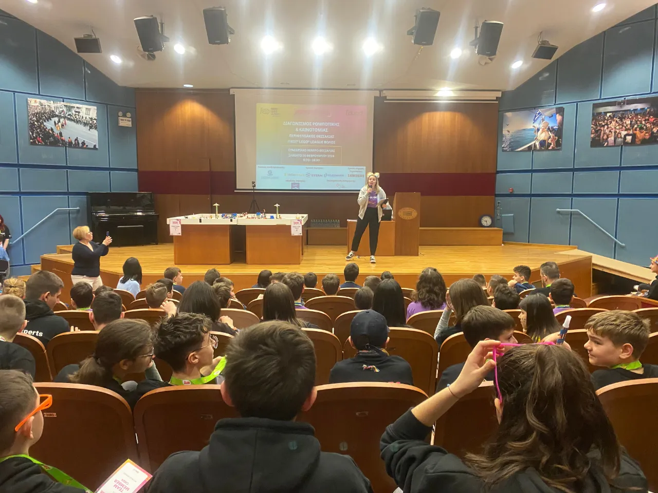 Η κεντρική παρουσιάστρια υποδέχεται όλες τις ομάδες και τους εθελοντές κατά την τελετή έναρξης του διαγωνισμού, σε ένα γεμάτο εμφιθέατρο